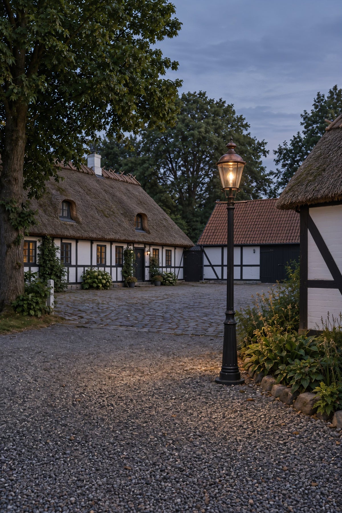 Stråtækt bindingsværksgård med standerlampe i kobber på gårdspladsen