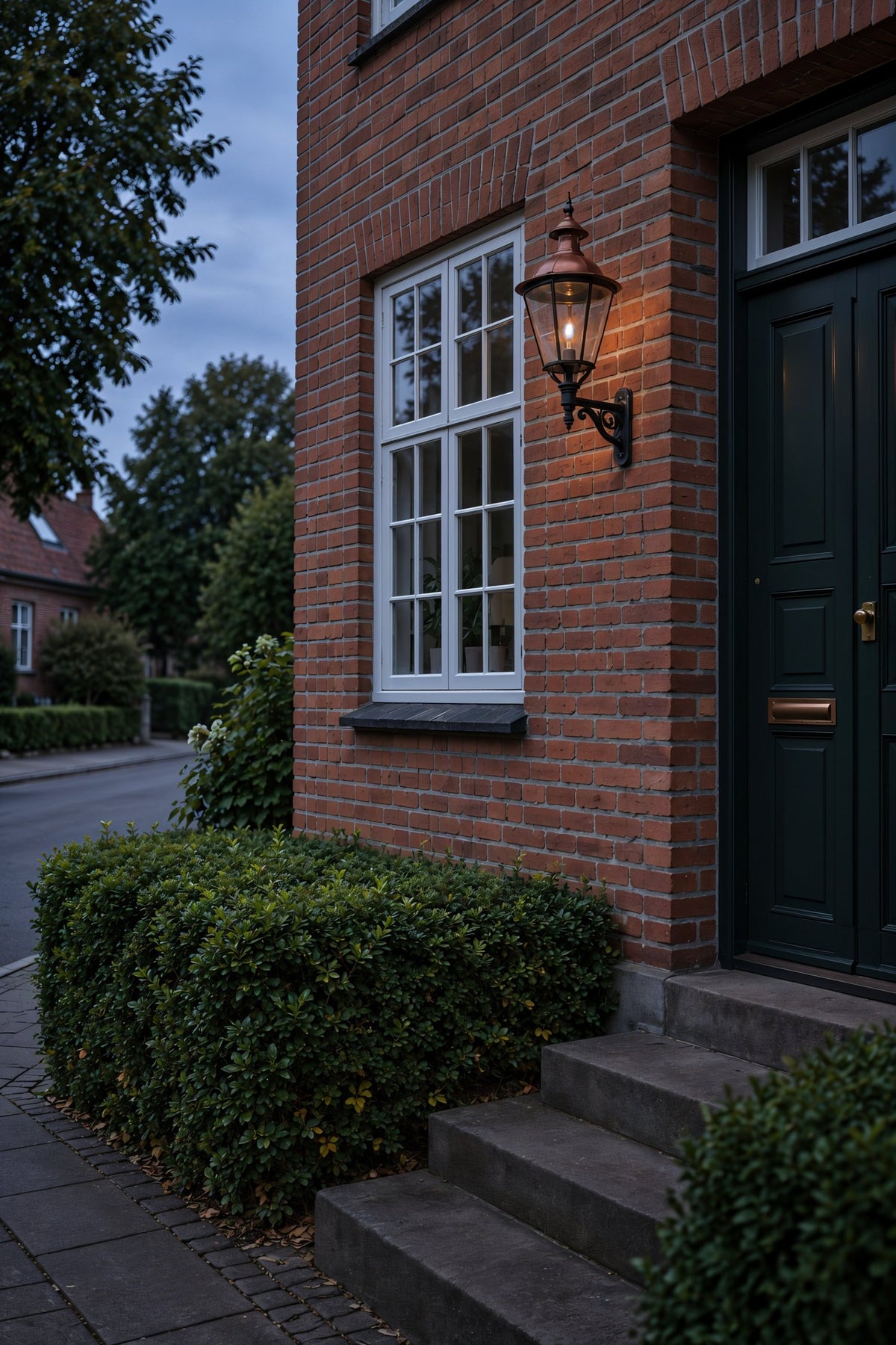 Rød murermestervilla i aftenlys med klassisk væglampe i kobber ved hoveddøren